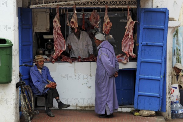 Men stand in front of a butcher shop in the souk of the old town of Essaouira, Essaouira, Morocco