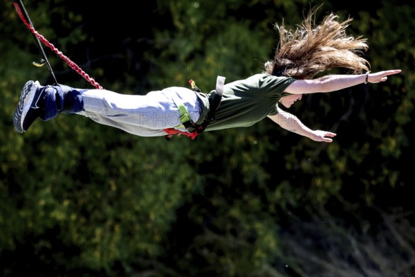 Female jumper in full length across the countryside bungee jumping, Queenstown, Otago, New Zealand