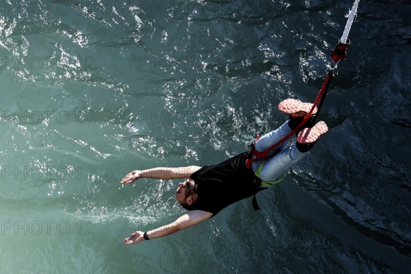 Person bungee jumping with arms extended over water, Queenstown, Kawarau Bridge, New Zealand
