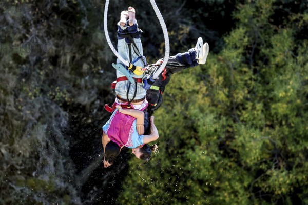 Two people in free fall bungee jumping surrounded by lush nature, Queenstown, Otago, New Zealand