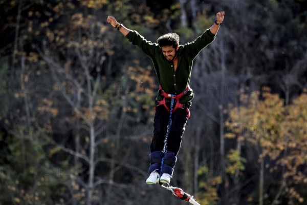 Person with arms spread out bungee jumping in front of autumn landscape, Queenstown, Otago, New Zealand