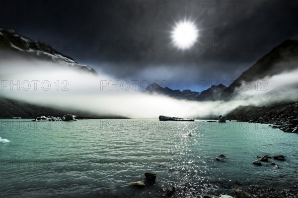 Turquoise glacial lake under bright sun and mystical fog