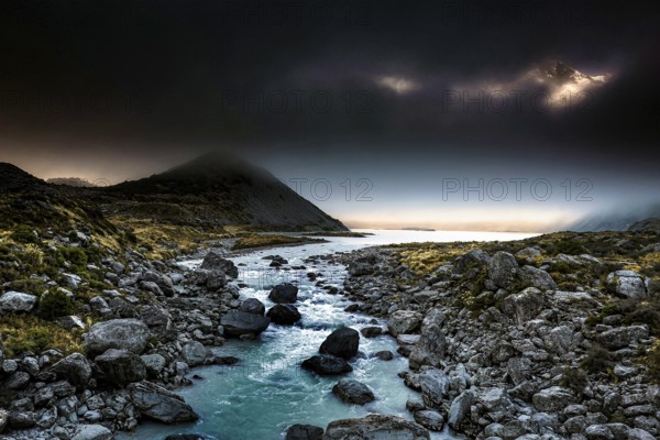 Dark mountain landscape with a narrow river surrounded by boulders in the evening light, Hooker Valley Track, New Zealand