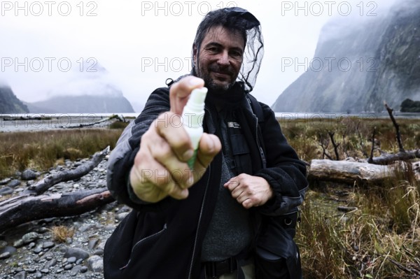 Man wearing outdoor clothes with mosquito repellent and head net in foggy mountain backdrop, Milford Sound, New Zealand