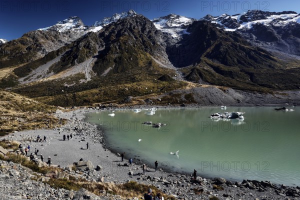 An expansive glacial lake surrounded by rugged mountains under clear skies, Mount Cook, New Zealand