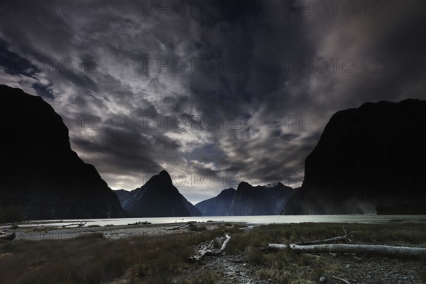 Dramatic clouds in the sky over Milford Sound at dusk, framed by silhouettes of mountains, zero