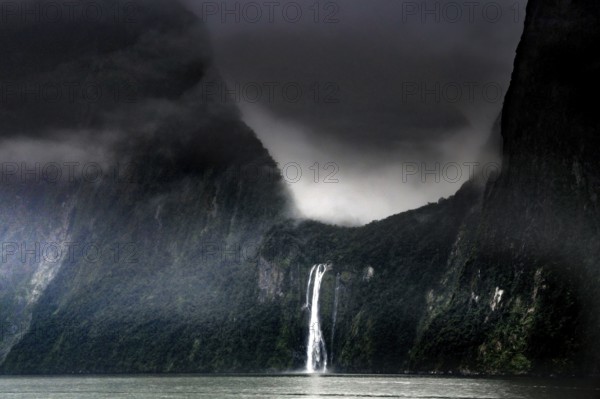 Dramatic sky over a waterfall in Milford Sound surrounded by misty mountains, zero