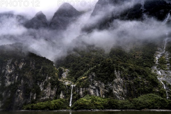 Foggy mountains and steep slopes in Milford Sound, surrounded by clouds and green vegetation, zero
