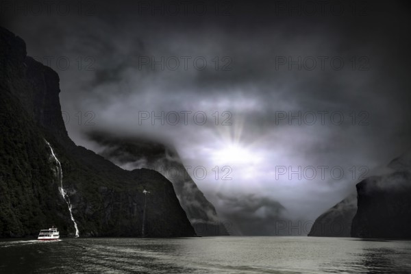Fjord landscape with a cruise ship, sun rays breaking through the cloud cover, Milford Sound, New Zealand