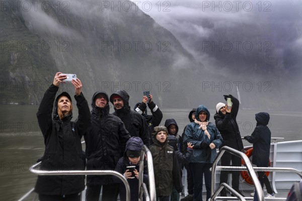 Group of passengers take pictures of the misty landscape from a cruise ship, Milford Sound, New Zealand