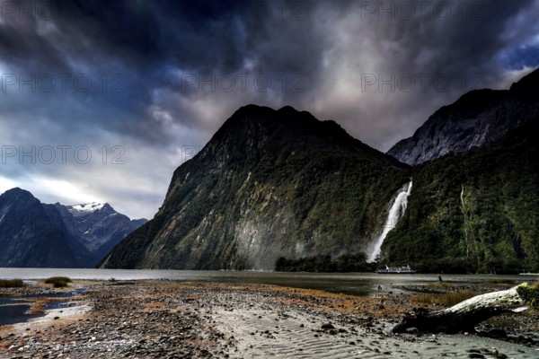 Dramatic landscape with waterfall ending in a fjord under a cloudy sky, Milford Sound, New Zealand
