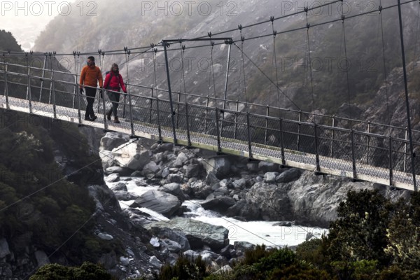 Hikers crossing a suspension bridge in a misty mountain landscape, Mt Cook, Hocker Valley Track, New Zealand
