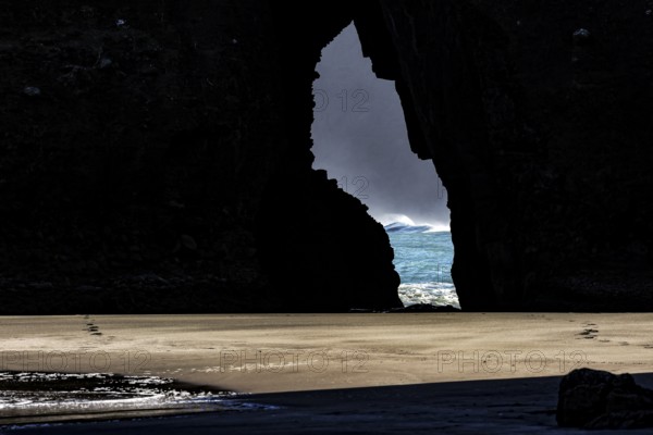 View through a crevice of the glowing sea at Piha Beach, Piha Beach, region, New Zealand