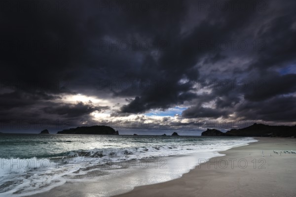 Dramatic sky over Hahei beach, dark clouds and rushing waves, Hahei, Coromandel Peninsula, New Zealand
