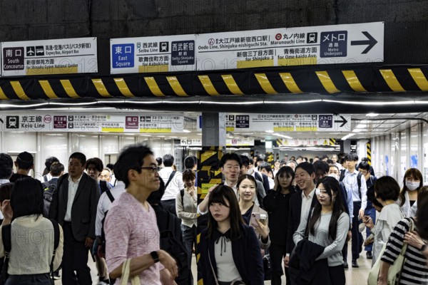 People flow through the busy train station surrounded by lots of signs, Tokyo, Japan