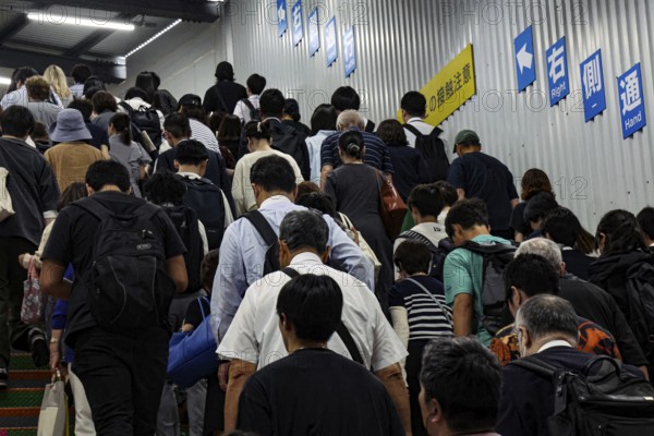 A crowd of people climbing a staircase in a train station surrounded by signs, Tokyo, Japan
