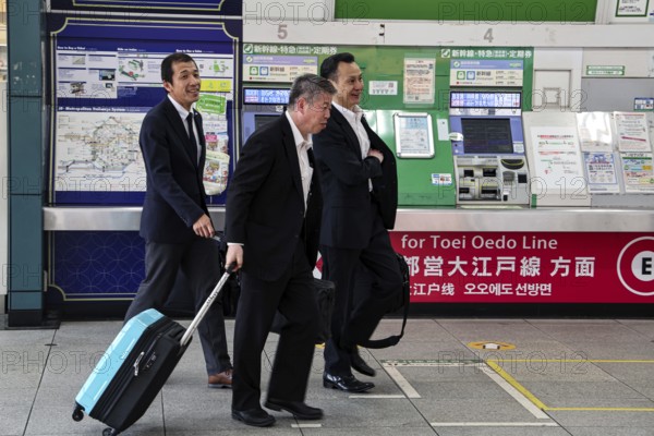 Salarimes with suitcases at train station, busy crossing, Tokyo, Japan