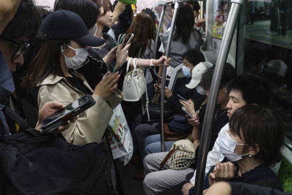Passengers on a full train, many wearing masks, Tokyo, Japan