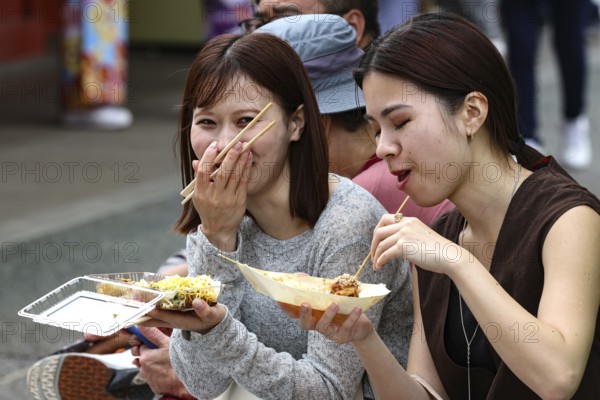 Two woman enjoy street food with chopsticks in Asakusa, Tokyo, Asakusa, Japan