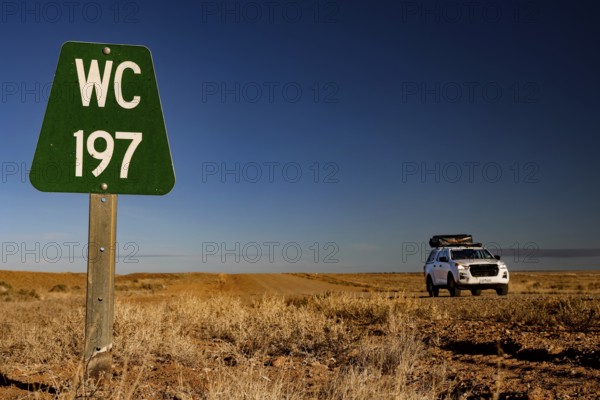A car and a green sign along a dusty road in the desert, zero