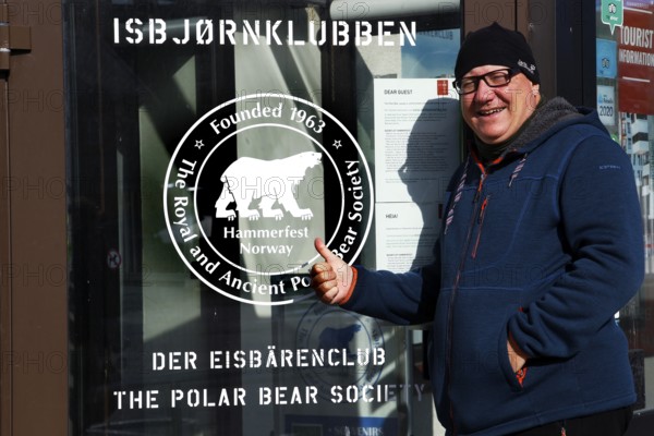A man poses in front of the entrance of Isbjornklubben, Hammerfest, Finnmark, Norway