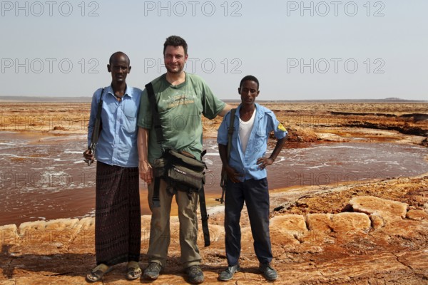 Three men stand at a hot spring in the desert of Dallol, Dallol, Ethiopia