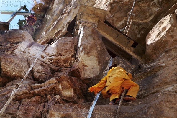A monk climbs a rope to the entrance on rocky ground, Debre Damo, Tigray, Ethiopia