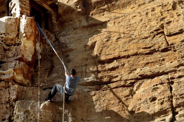 Person climbing a steep rock wall with rope to the entrance, Debre Damo, Tigray, Ethiopia