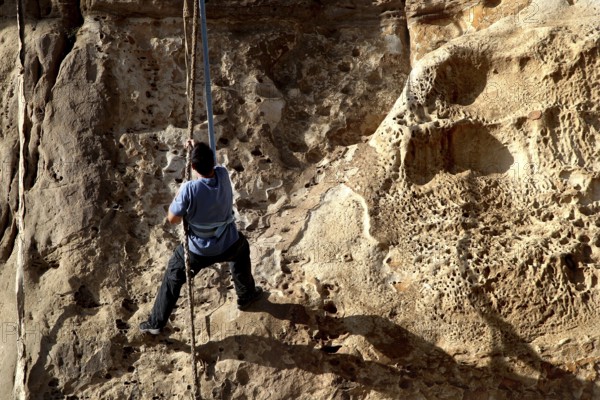 Person climbing a steep rock wall with rope, Debre Damo, Tigray, Ethiopia