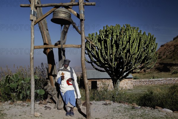 Priest next to a bell near the rock church Debre Mariam Krokor, zero