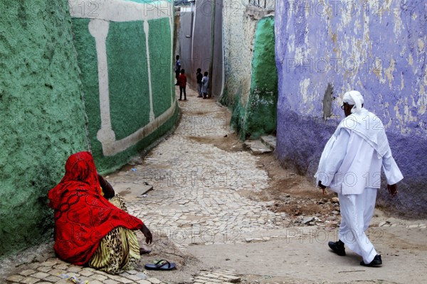 Two people wearing traditional clothes in a colorful alley in Harar, Harar, Ethiopia