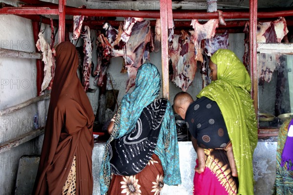 Women in colorful hijabs stand in front of a butcher shop in Harar, Harar, Oromia, Ethiopia