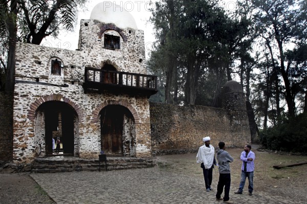Stone gate building with arched windows and people surrounded by trees