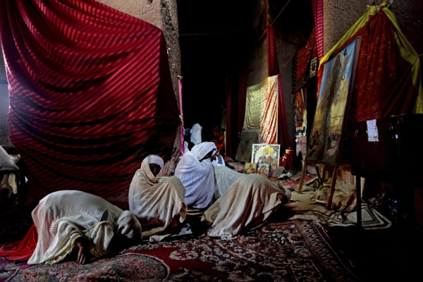 Interior view of Bete Marqorewas with praying people in rich colors, Lalibela, Amhara, Ethiopia
