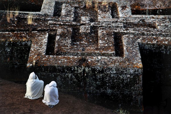 Two veiled pilgrims pray in front of the impressive Bete Gyorgis, Lalibela, Amhara, Ethiopia