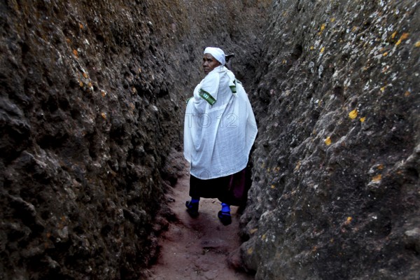 A person wearing traditional clothing walks through a narrow rocky passage near Bete Gyorgis, Lalibela, Amhara, Ethiopia