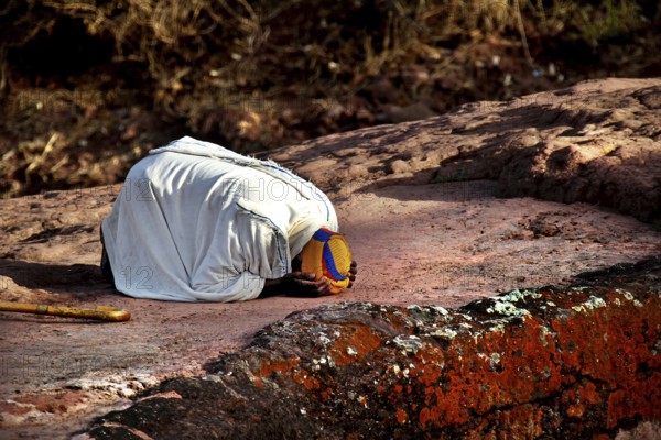 Kneeling person praying on rock, expressing deep faith near Bete Gyorgis, Lalibela, Amhara, Ethiopia