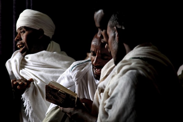 Men read Bete Gabriel and Raphael in the dark church, engrossed in prayer, Lalibela, Amhara, Ethiopia