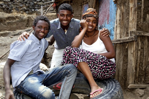 Three laughing people in a rural area in front of a wooden hut, Lalibela, Ethiopia