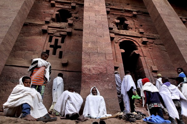 Pilgrims wearing white cloaks gather solemnly in front of the Bete Medhane Alem rock church at Easter, Lalibela, Amhara, Ethiopia