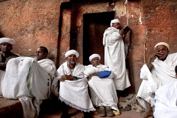 A group of men sitting on a stone wall wearing traditional clothing, Lalibela, Amhara, Ethiopia