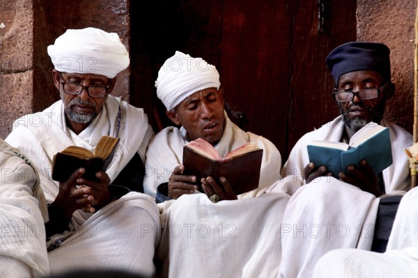 Three men in traditional clothes read books together, Lalibela, Amhara, Ethiopia