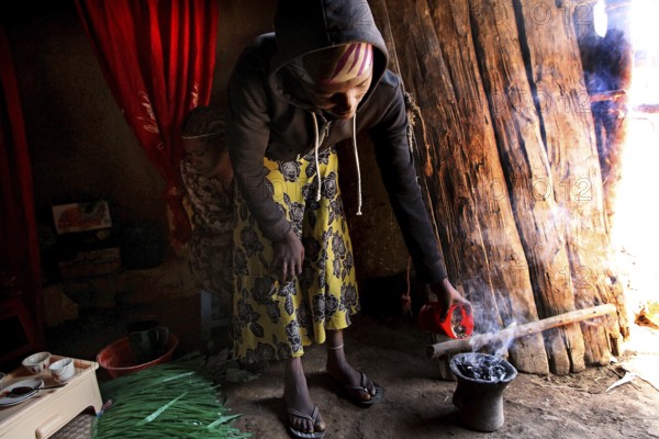 Lady carefully performs the coffee ceremony in her cozy abode. Smoke rises, Lalibela, Amhara, Ethiopia