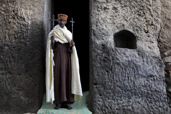 Priest with crosses standing in stone niche, Lalibela, Lasta Mountains, Ethiopia