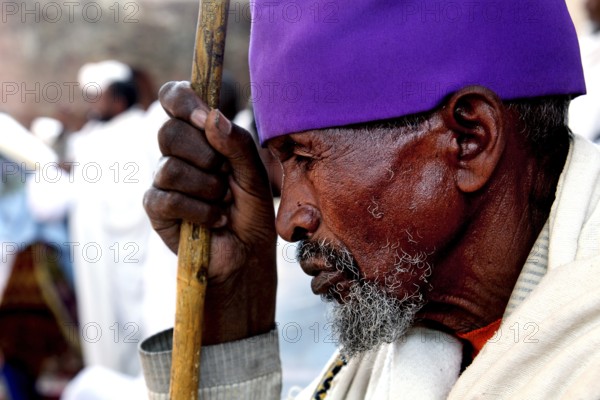 An elderly man wearing purple head covering prays at Bete Maryam church during Easter, Lalibela, Amhara, Ethiopia