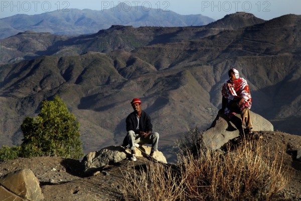 Two people sit in front of the impressive mountain scenery of the Lasta Mountains, Lalibela, Amhara, Ethiopia