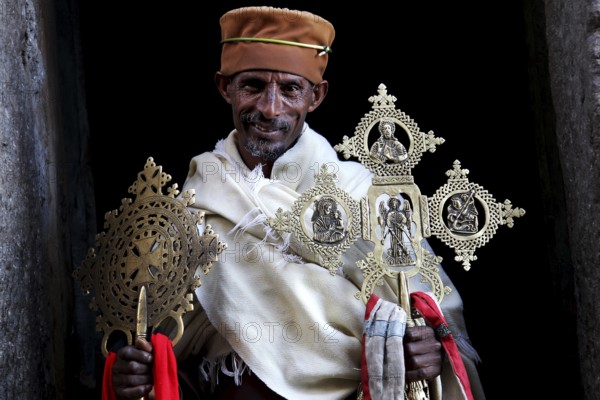 Priest with decorative crosses in traditional robes against dark background, Lalibela, Lasta Mountains, Ethiopia