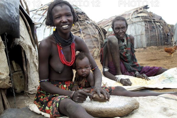 Woman grinds corn in a traditional settlement in Omorate, friendly atmosphere, Omorate, Ethiopia