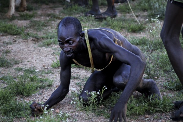 A man kneels exhausted on the ground during the initiation ritual, Turmi, Ethiopia