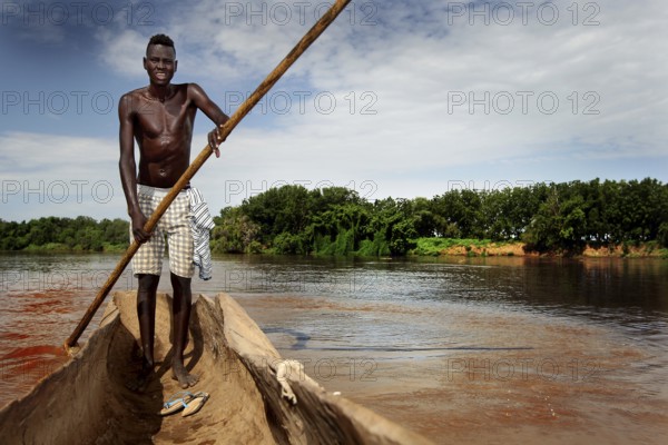 Man navigates in a dugout along the Omo River, surrounded by thick vegetation, Omorate, Ethiopia